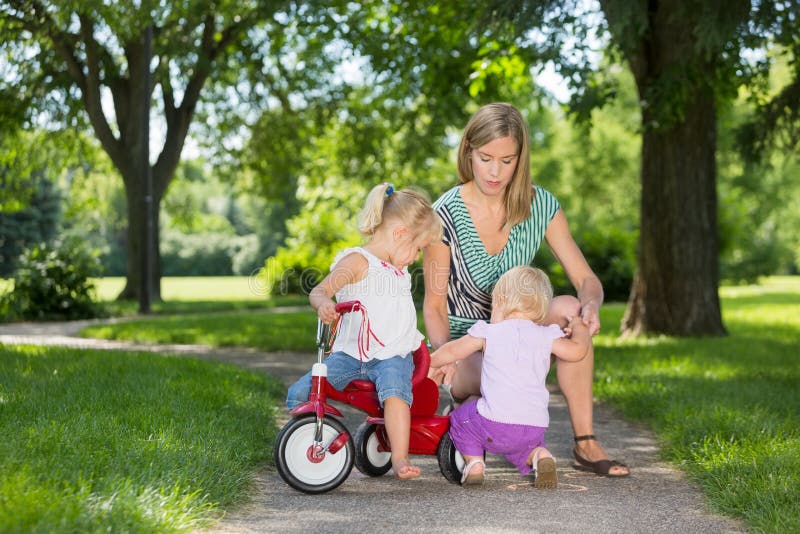 Mère et enfants avec le tricycle en parc photo stock Mère et enfants avec le tricycle en parc photo stock