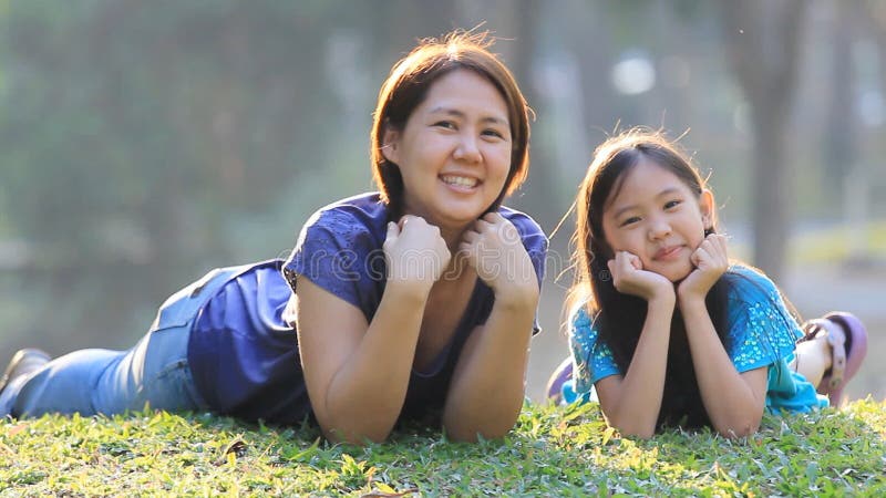 Mère et fille asiatiques heureuses sur l'herbe au jour d'été ensoleillé en parc