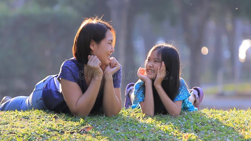 Mère et fille asiatiques heureuses sur l'herbe au jour d'été ensoleillé en parc