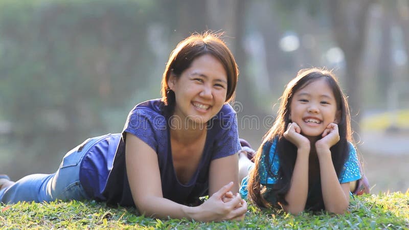 Mère et fille asiatiques sur l'herbe au jour d'été ensoleillé en parc