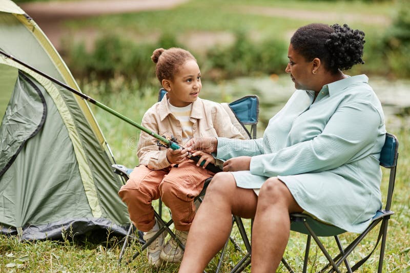 Mère et fille campant ensemble à l'extérieur et tenant une canne à pêche photos stock