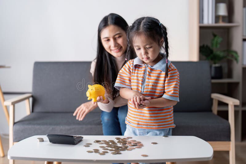 Mère et fille comptant les pièces ensemble tout en apprenant à économiser de l'argent dans un salon moderne. photo libre de droits