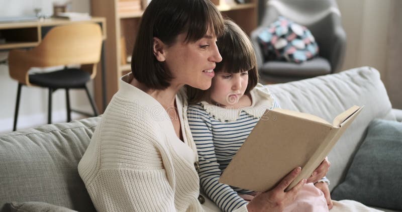 Mère et fille lisant un livre sur le canapé du salon banque de vidéos