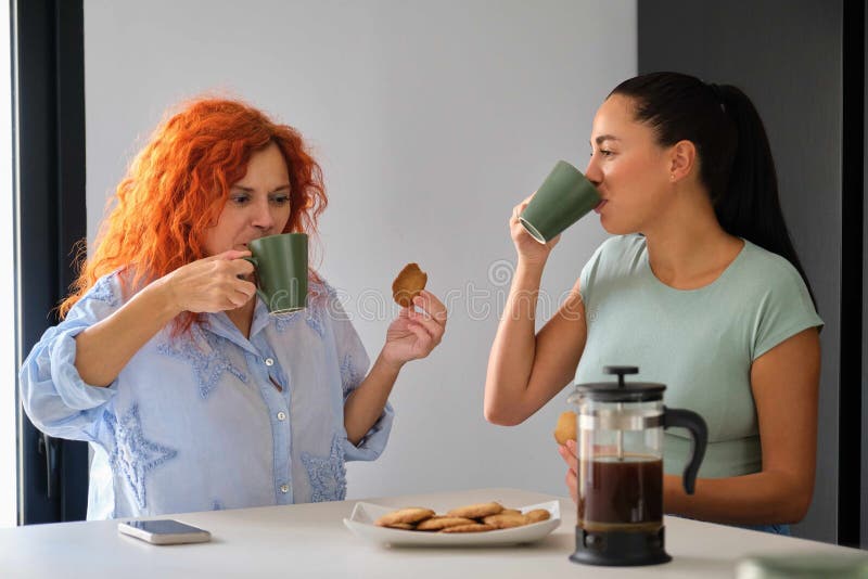 Mother and daughter drinking coffee while having breakfast together in the morning. Family time. Mother and daughter drinking coffee while having breakfast together in the morning. Family time.