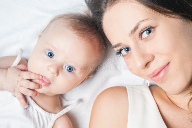 Mère heureuse avec un bébé se trouvant sur un lit blanc photographie stock Mère heureuse avec un bébé se trouvant sur un lit blanc photographie stock
