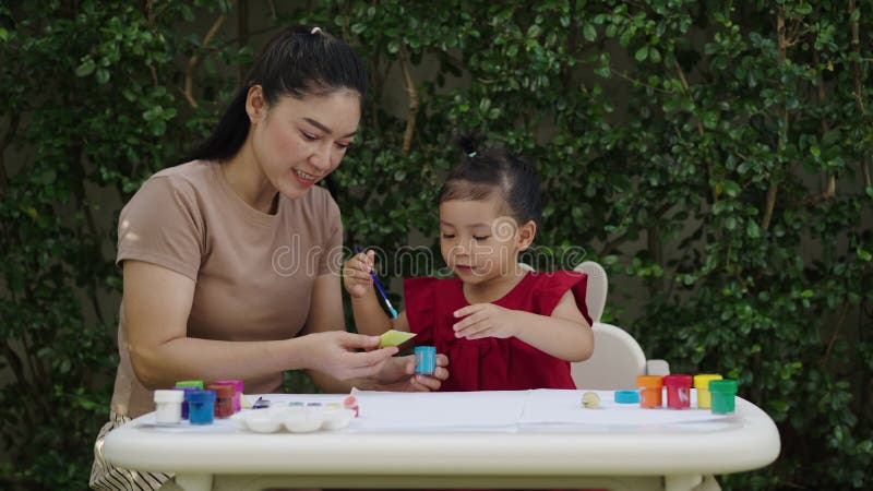 Mère heureuse et petite fille peignant de l'aquarelle à partir d'un bananier en papier dans le jardin. clips vidéos
