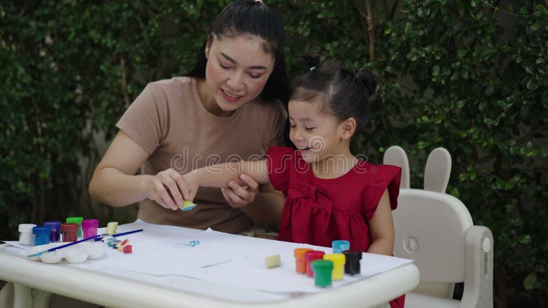 Mère heureuse et petite fille peignant de l'aquarelle à partir d'un bananier en papier dans le jardin. banque de vidéos