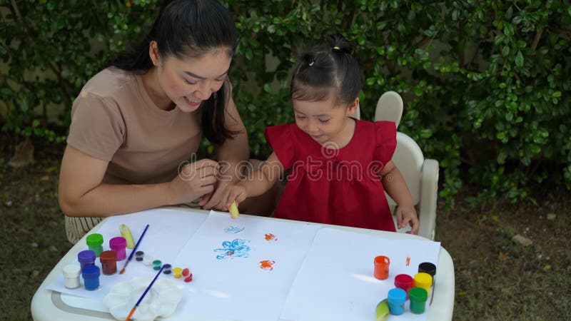 Mère heureuse et petite fille peignant de l'aquarelle à partir d'un bananier en papier dans le jardin. banque de vidéos