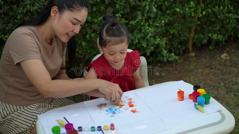 Mère heureuse et petite fille peignant de l'aquarelle à partir d'un bananier en papier dans le jardin. banque de vidéos