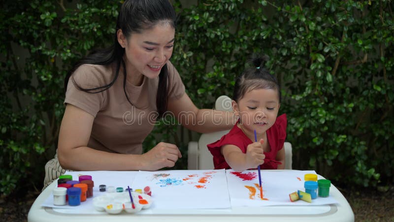 Mère heureuse et petite fille peindre l'aquarelle dans le papier dans le jardin banque de vidéos