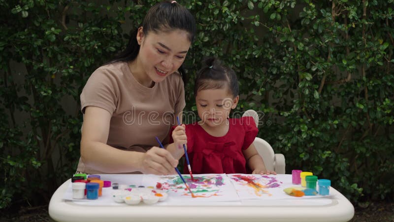 Mère heureuse et petite fille peindre l'aquarelle dans le papier dans le jardin banque de vidéos