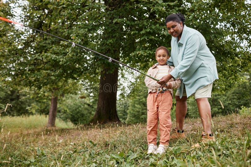 Mère noire heureuse enseignant petite fille pêche dehors image stock