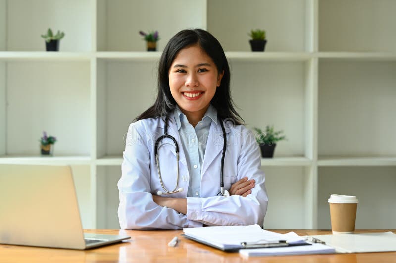 Confident fe doctor wearing white uniform sitting with arms crossed and smiling to camera. Confident fe doctor wearing white uniform sitting with arms crossed and smiling to camera.