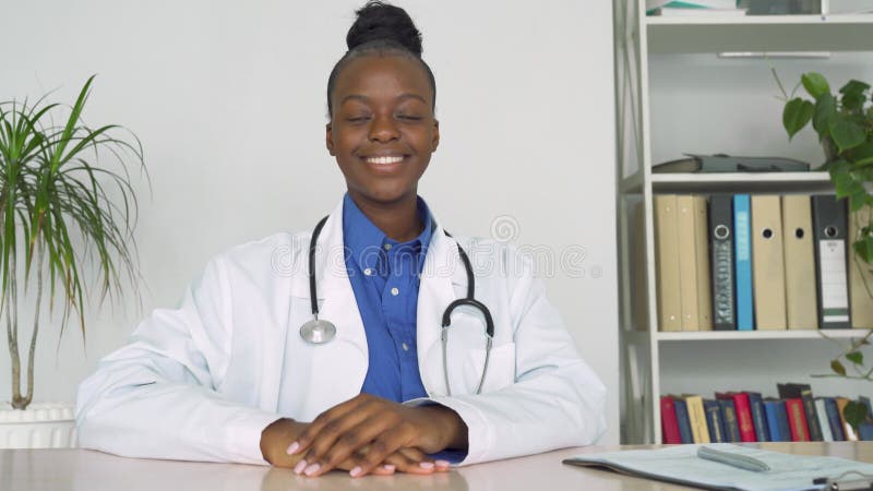 Médecin féminin de sourire sûr d'afrique à regarder la caméra reposant sur le lieu de travail. banque de vidéos