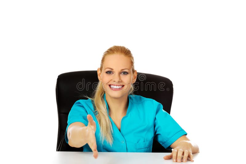 Médecin ou infirmière féminin de sourire s'asseyant derrière le bureau avec la main redy à la poignée de main image libre de droits Médecin ou infirmière féminin de sourire s'asseyant derrière le bureau avec la main redy à la poignée de main image libre de droits