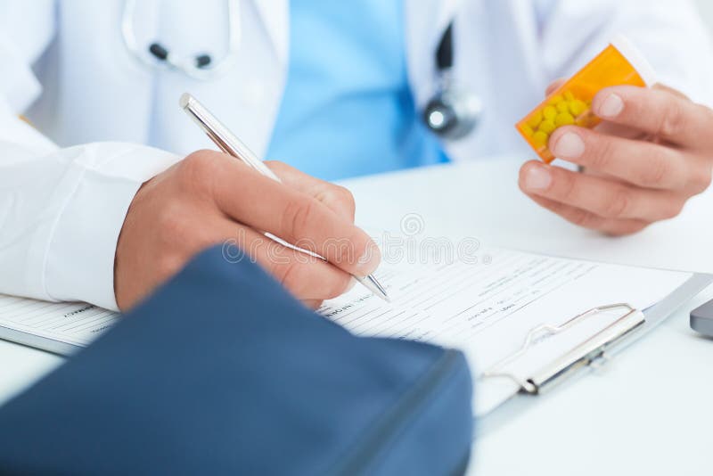 Médecin ou pharmacien masculin de médecine de médecin s'asseyant à la table de travail, tenant le pot ou la bouteille de pilules photographie stock Médecin ou pharmacien masculin de médecine de médecin s'asseyant à la table de travail, tenant le pot ou la bouteille de pilules photographie stock