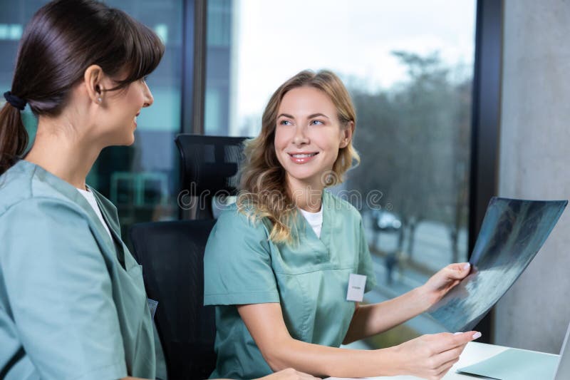 Médica sosteniendo una imagen de xray mientras discute el diagnóstico de la enfermedad ósea con un colega fotografía de archivo