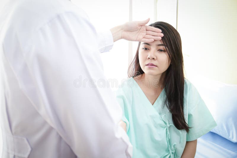 An Asian male doctor uses the back of her hand to hold the forehead of a female patient. To check the body heat temperature. The concept of health examination and medical services in hospitals. An Asian male doctor uses the back of her hand to hold the forehead of a female patient. To check the body heat temperature. The concept of health examination and medical services in hospitals