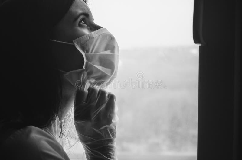 Médico cansado con una máscara médica y guante de protección cerca de la ventana fotografía de archivo libre de regalías