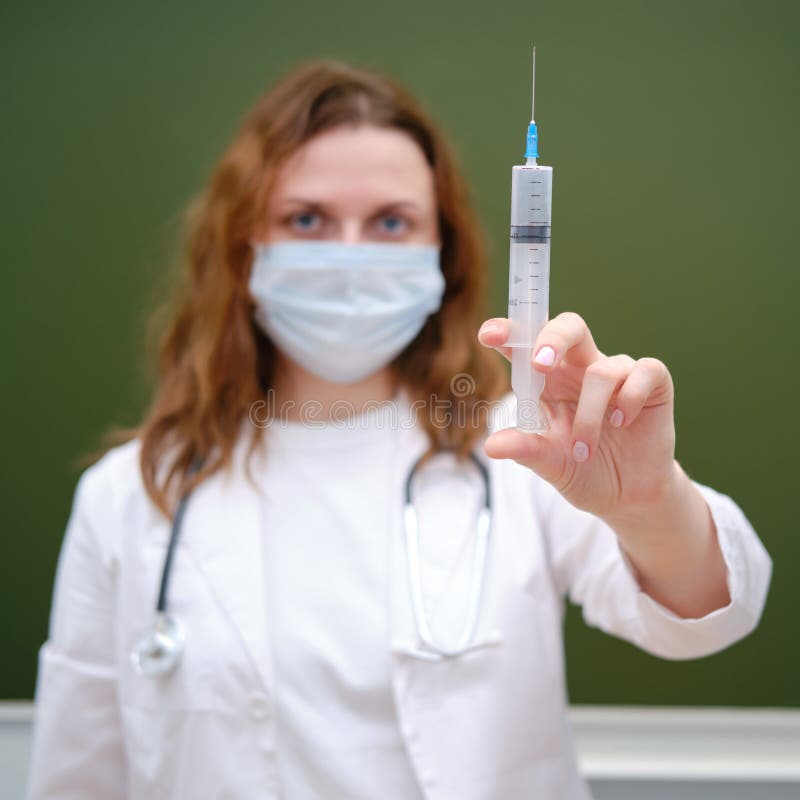 Doctor with a large syringe for vaccination in a school class. The problem with lessons in the classroom during the virus outbreak. Doctor with a large syringe for vaccination in a school class. The problem with lessons in the classroom during the virus outbreak..