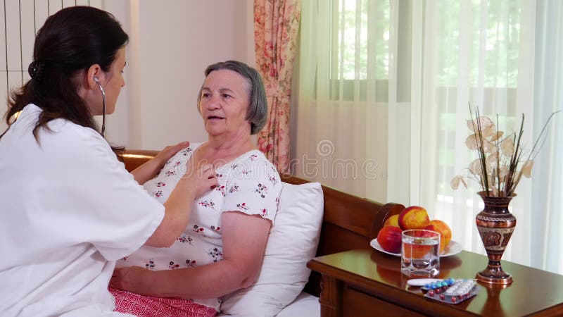 Médico de família que verifica a mulher superior que usa o estetoscópio em casa