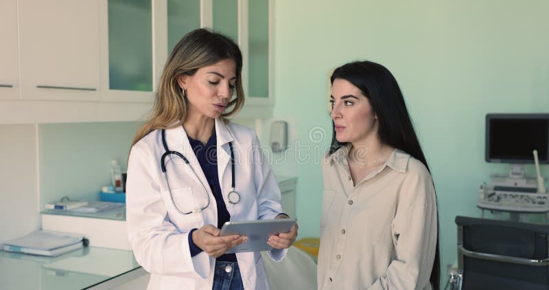 Médico hispano joven mostrando la pantalla del comprimido a una paciente femenina almacen de video
