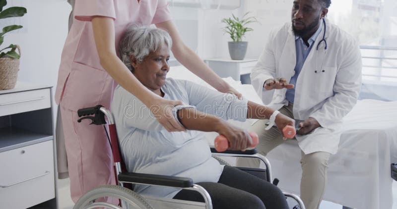 Médico masculino diverso y fisioterapeuta femenino tratando a pacientes de edad avanzada en cámara lenta en silla de ruedas almacen de metraje de vídeo