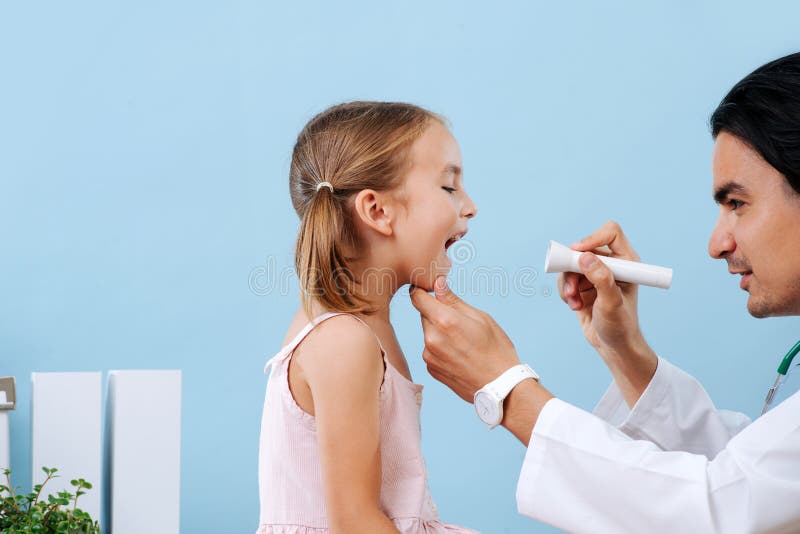 Médico masculino examinando as amÃdalas das meninas no hospital, usando lanterna imagens de stock Médico masculino examinando as amÃdalas das meninas no hospital, usando lanterna imagens de stock