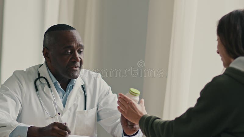 Médico profesional terapeuta hombre africano oftalmólogo ginecólogo consultar a una clienta mujer con enfermedad de escritura en e almacen de metraje de vídeo