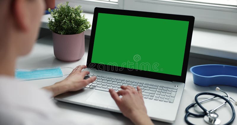 Médico que trabaja en laptop en el consultorio de la clínica. ordenador con pantalla verde