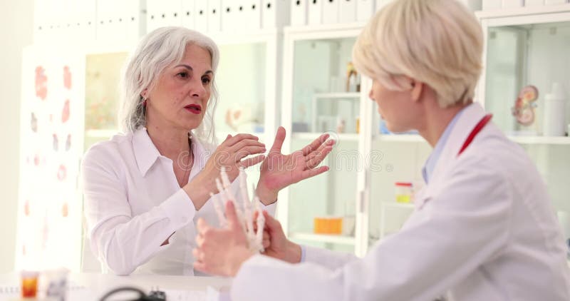 Médico reumatologista mostrando o modelo anatômico da mão humana para a mulher idosa com filme de artrite reumatoide 4k lento