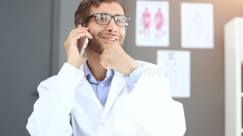 Médico varón cercano con uniforme blanco sostiene smartphone navegar por internet en la clínica. almacen de video