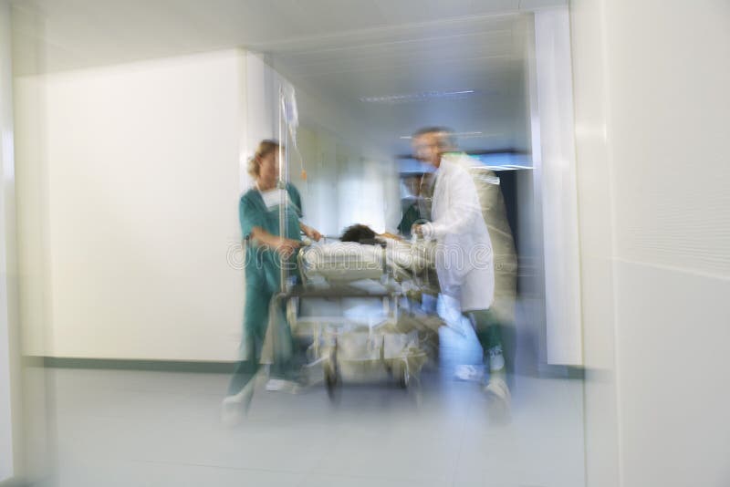 Médicos que mueven al paciente en la camilla a través del pasillo del hospital fotografía de archivo Médicos que mueven al paciente en la camilla a través del pasillo del hospital fotografía de archivo