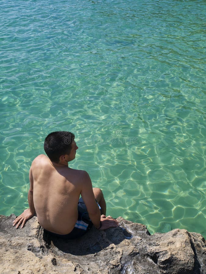 Young man sitting in a rock in the idyllic beach of Cala Fornells, Mallorca. Young man sitting in a rock in the idyllic beach of Cala Fornells, Mallorca