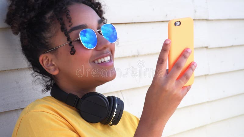 Métis afro-américaine jeune femme portant des lunettes de soleil utilisant le téléphone portable pour les médias sociaux banque de vidéos