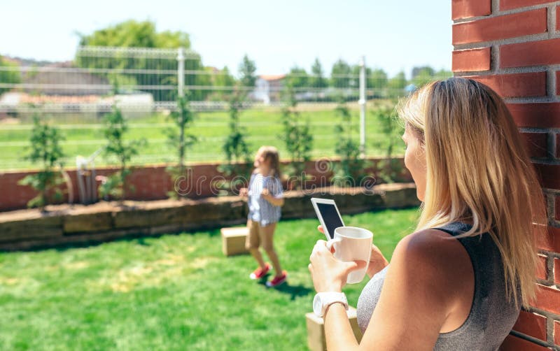 Móvil de observación de la madre mientras que el hijo juega fotografía de archivo Móvil de observación de la madre mientras que el hijo juega fotografía de archivo