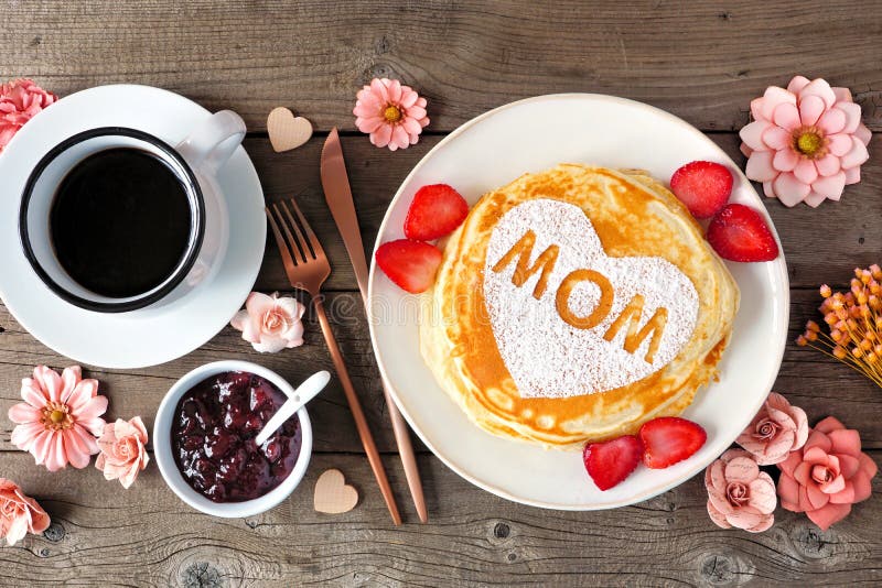 Mödrar dag frukostpannkakor med hjärtform och moderbokstäver i bordsmiljö på rustiskt trä