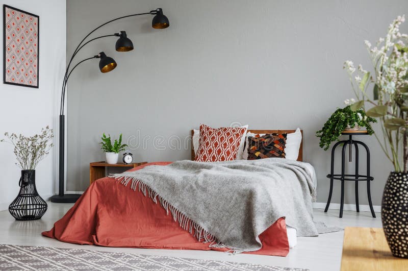 Mönstrad kudde och grå filt på konungformatsäng med mörkt - orange duntäcke i det lyxiga sovrummet som är inre i elegant lägenhet royaltyfria foton