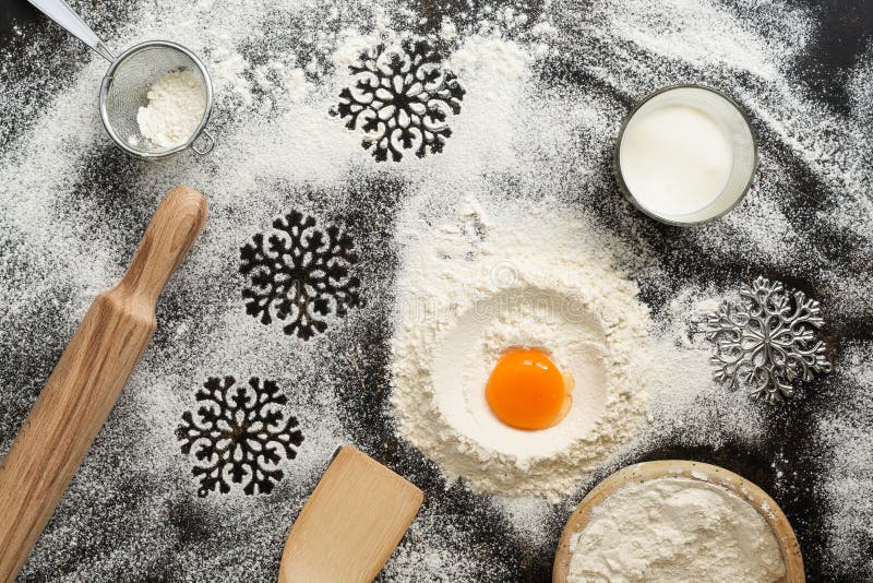 Mörk bakgrund för jul med att baka ingredienser Mjöl ägg, mjölkar, kavlen, sikten, snöflingor, spatel Bästa sikt, ställe för arkivfoto Mörk bakgrund för jul med att baka ingredienser Mjöl ägg, mjölkar, kavlen, sikten, snöflingor, spatel Bästa sikt, ställe för arkivfoto