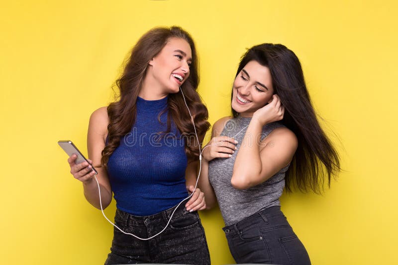Música de escuta de duas mulheres em linha no smartphone imagens de stock royalty free Música de escuta de duas mulheres em linha no smartphone imagens de stock royalty free