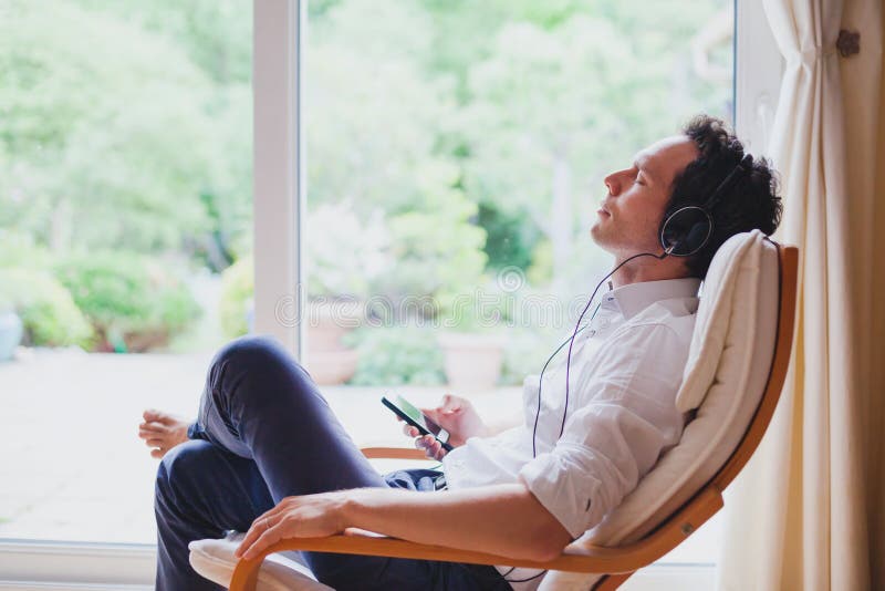 Música relajante que escucha en casa, hombre relajado en los auriculares que se sientan en silla de cubierta