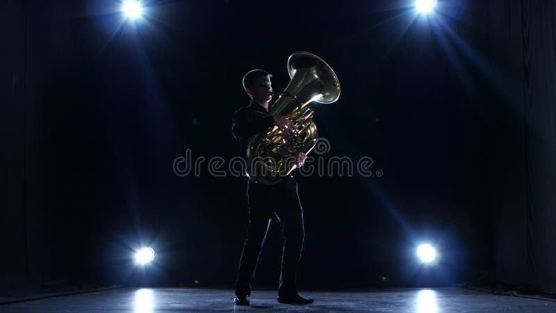 Músico en estudio oscuro con los proyectores que juegan jazz lento de la tuba