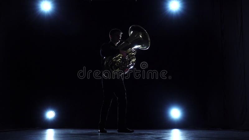 Músico en oscuridad con los proyectores que juegan jazz de la tuba Cámara lenta