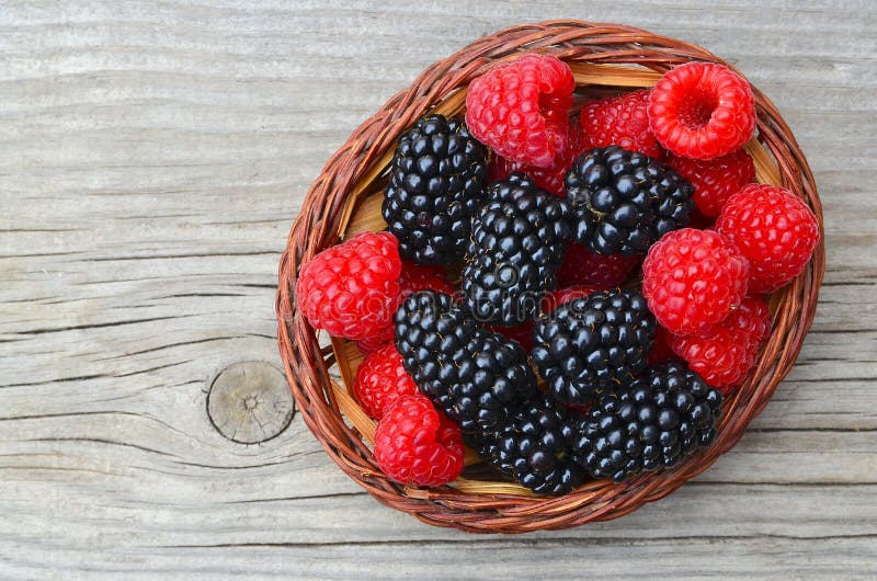 Mûres et framboises organiques fraîchement sélectionnées dans un panier sur la vieille table en bois photo stock Mûres et framboises organiques fraîchement sélectionnées dans un panier sur la vieille table en bois photo stock
