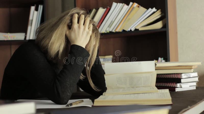 Müder Student, der in der Bibliothek im College studiert Die Studentin, die am Schreibtisch sitzt und ergreift ihren Kopf