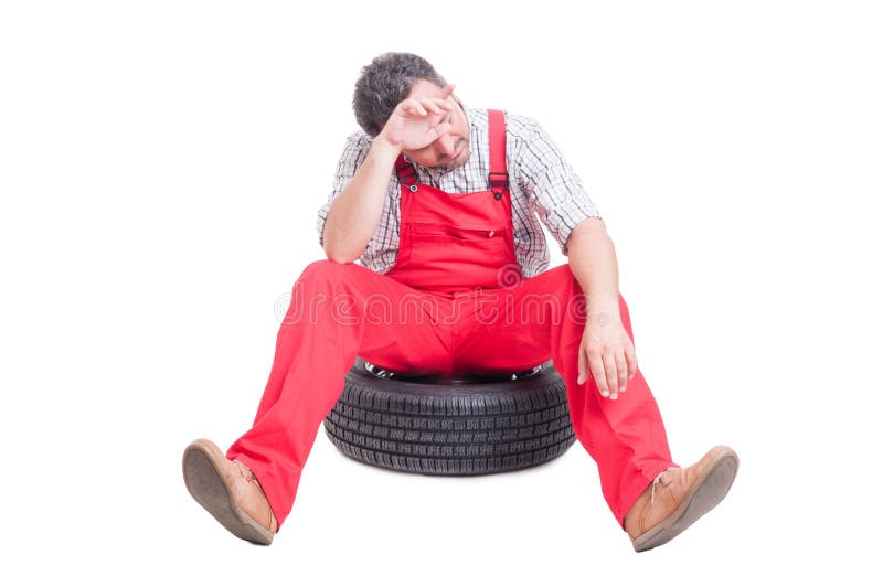 Müder und erschöpfter Mechaniker, der auf einem Autorad sitzt stockfotografie Müder und erschöpfter Mechaniker, der auf einem Autorad sitzt stockfotografie