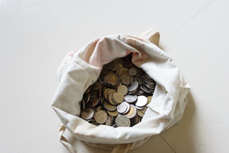 The hands are piked up silver coins into the old bag white,with white background ,image focus on a coin cells. The hands are piked up silver coins into the old bag white,with white background ,image focus on a coin cells