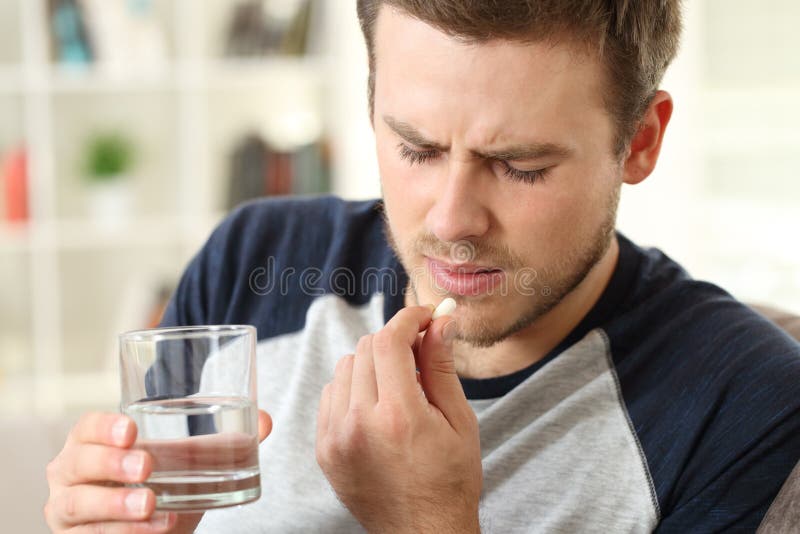 Man suffering taking a pill sitting on a sofa in the living room in a house interior. Man suffering taking a pill sitting on a sofa in the living room in a house interior