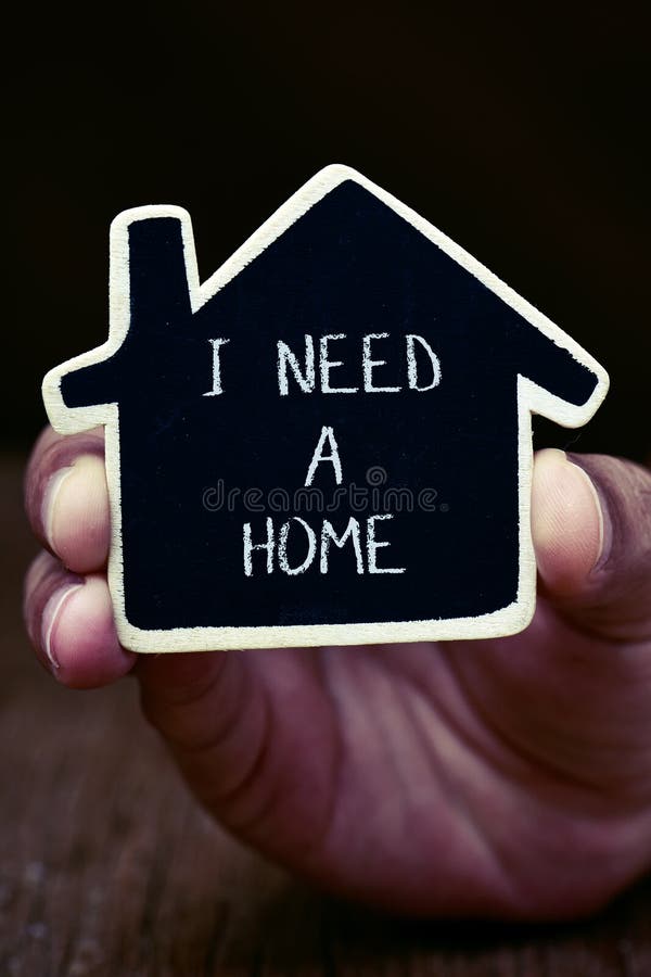 Closeup of the hand of a young man showing a black house-shaped signboard wtih the text I need a home. Closeup of the hand of a young man showing a black house-shaped signboard wtih the text I need a home