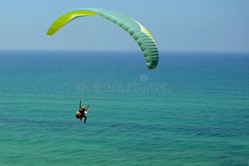 Mężczyzna lata na zielonym paraglider w niebie nad lazurowy morze Równowaga, krańcowi sporty, styl życia Morze Śródziemnomorskie